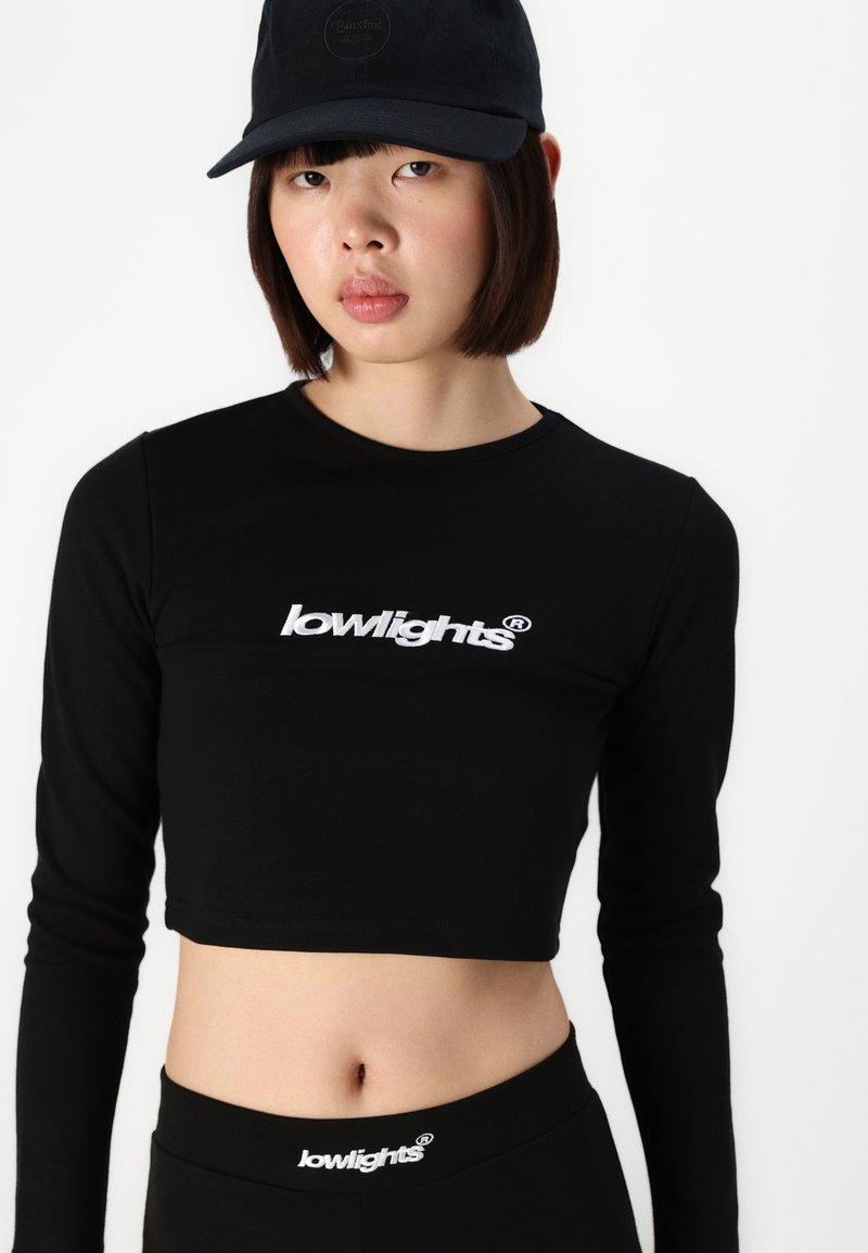 Black long-sleeve cropped top with "lowlights" logo in white. Paired with black high-waisted bottoms. Both garments are fitted and smooth-textured.