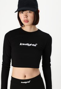 Black long-sleeve crop top with a round neckline, featuring white embroidered logo on the chest. Paired with black high-waisted leggings.