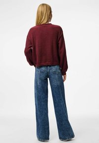 Bordeauxfärgad kort tröja med långa ärmar som är kombinerad med vida blå denimjeans. Mjuk tygtextur med en avslappnad passform och rak skärning.