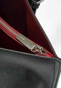 Wnętrze czarnej skórzanej torby na ramię z czerwonym wykończeniem i srebrnym zamkiem błyskawicznym. Ciekawe detale obejmują fakturowany materiał oraz kontrastowe przeszycia.