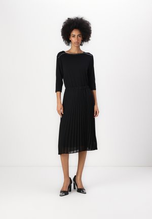 Zwarte geplisseerde midi-jurk met een ronde halslijn en driekwartmouwen, voorzien van decoratieve studs langs de schouders.