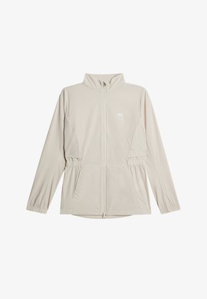 Lichtbeige jas met ritssluiting, lange mouwen, elastische manchetten, zijzakken, een opstaande kraag en een klein wit logo op de borst.