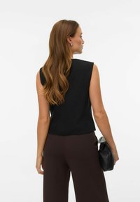 Mustad varrukateta top, millel on struktureeritud õlad, kombineeritud tumepruunide laia säärega pükstega. Käes on tekstuuriga must käekott. Siidine kangas.