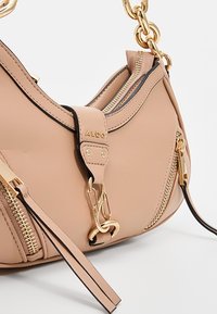 Sac à main en cuir beige avec poignée chaîne dorée, détails de fermeture éclair, et logo de la marque ALDO sur la sangle avant avec des accents métalliques dorés.