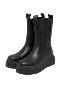 Botas de tobillo de cuero negro con paneles laterales elásticos y tiradores. Suela de goma gruesa y acanalada para tracción y altura. Logo "BUFFALO" en el lateral.