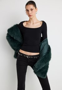 Sort langærmet top med firkantet halsudskæring, kombineret med en mørkegrøn jakke i imiteret pels. Sorte jeans med bælte med store metaløjer.
