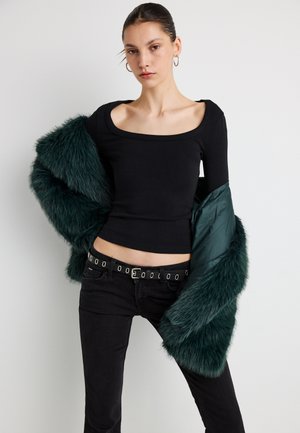 Zwart top met lange mouwen en een vierkante halslijn, gecombineerd met een donkergroene jas van nepbont. Zwarte jeans met een riem met grote metalen oogjes.