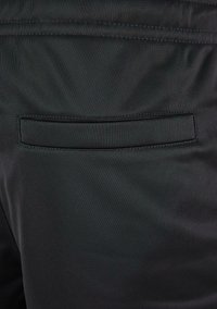 Detaliu cu buzunar din țesătură neagră pe pantaloni, având o deschidere orizontală cu margini cusute, evidențiind o textură netedă și un design minimalist.