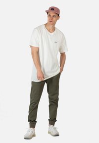 Witte katoenen t-shirt met een klein logo, olijfgroene joggers en een lichtroze pet. Lichte sneakers met een gestructureerde zool.