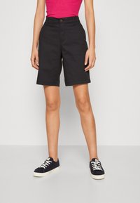 Zwarte katoenen shorts met rechte snit, voorste knoopsluiting en achterzakken, gecombineerd met marineblauwe sneakers en een roze aangesloten top.