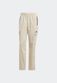 Pantalones cargo beige con cintura elástica, bolsillos laterales con cremalleras y un detalle de parche en la pierna izquierda. Fabricados en tela ligera.