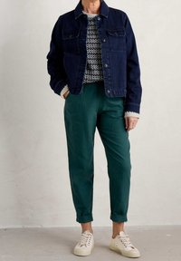 Donkerdenim jack, gebreid trui met patroon, groene tapered broek en beige sneakers. Jack met twee borstzakken en opgerolde mouwen.