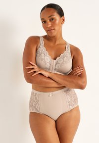 Beige bh med spetsdetaljer och V-ringning, samt matchande högmidjade trosor med spetskanter och en liten rosett i mitten.