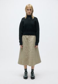 Sweater de fleece preto com gola alta, saia midi em quilted caqui e sapatos de caminhada pretos com detalhes cinzentos; fundo simples.