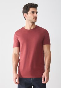 Red cotton T-shirt with a round neckline and short sleeves, displayed on a model, paired with dark denim jeans. Smooth texture.
