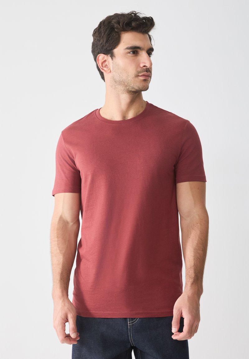 T-shirt en coton rouge avec un col rond et des manches courtes, présenté sur un modèle, associé à un jean en denim foncé. Texture lisse.