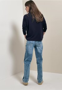 Top de manga larga azul marino combinado con jeans rectos de un azul claro, con bolsillos traseros y calzado beige. Diseño sencillo, ajuste casual.
