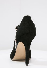 Černá semišová dámská vysoká bota na podpatku s špičatou špičkou, kotníkovým páskem se stříbrnou sponou a štíhlým podpatkem. Jednoduchý, elegantní design.