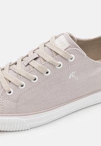 Ljust rosa canvas sneakers med beige snörning, vita ögonhål och en vit gummisula. Har en logotyp på sidan och en texturerad tånäsa.