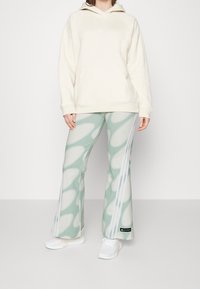 Vit huvtröja med en lös passform, i kombination med mintgröna utsvängda byxor med ett vitt abstrakt mönster och sidostriper. Vita sneakers.