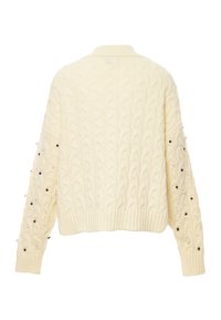 Krämfärgad kabelstickad tröja med en kortad design, med texturerade mönster och prydnadsärmar med svarta och vita pärlor. Handstickad look.
