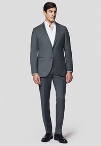 Szary garnitur w prążki o dopasowanym kroju, marynarka na jeden guzik i klapy, w zestawie z białą koszulą i wypastowanymi czarnymi butami.