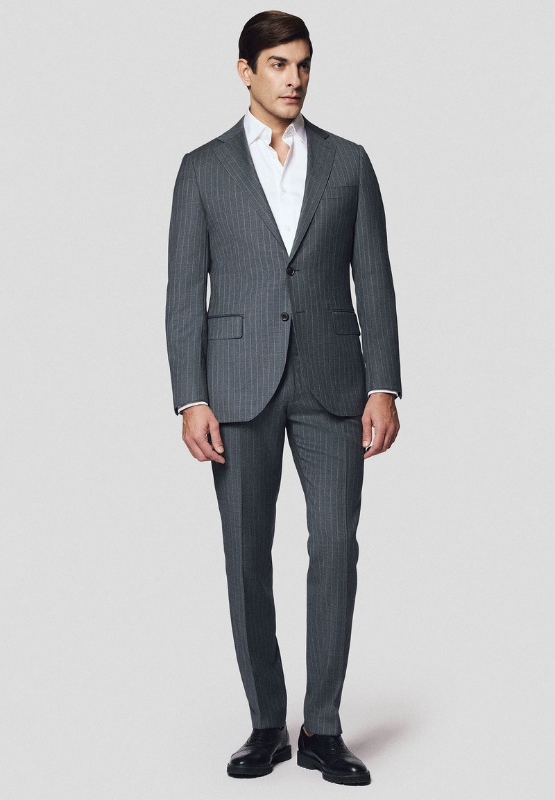 Szary garnitur w prążki o dopasowanym kroju, marynarka na jeden guzik i klapy, w zestawie z białą koszulą i wypastowanymi czarnymi butami.