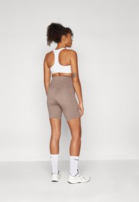 Brune treningsshorts og en hvit sports-bh. Shortsene har høy livvidde og sidelommer. Hvite sokker og joggesko fullfører antrekket.