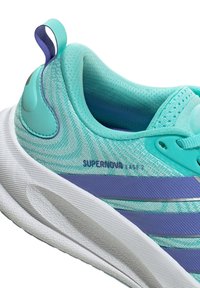 Nahaufnahme eines türkisfarbenen und lila Adidas Supernova Ease 2 Laufschuhs mit weißer strukturierter Sohle und gepolstertem Schaft.
