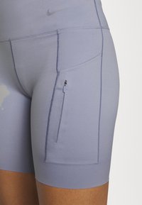 Primo piano di shorts atletici viola con tasca laterale con zip e cuciture visibili sulla coscia di una persona.