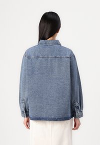 Jeans jakna u svijetloplavoj boji, s opuštenim krojem, dugmadima na rukavima i leđnim jatom. Jednostavan dizajn bez uočljivih uzoraka ili akcenata.