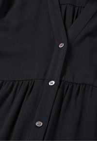 Schwarzes knopfbares Kleid mit V-Ausschnitt, weichem Stoff, geraffter Taille und zwei silbernen Knöpfen auf der Vorderseite.