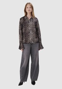 Koszula w panterkę z kołnierzykiem i rozkloszowanymi rękawami, w zestawie z wysokim stanem szarymi spodniami o szerokich nogawkach i czarnymi botkami za kostkę.