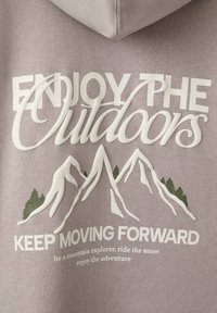 Felpa grigia con testo bianco e verde e grafiche di montagne. Il testo recita: "GODITI L'OUTDOOR CONTINUA A PROGREDIRE" con dettagli sottostanti.