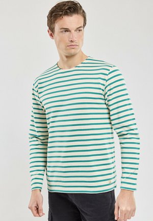 T-shirt à manches longues rayé en crème et vert, avec un col rond et un petit logo sur le bas. Matière en coton.