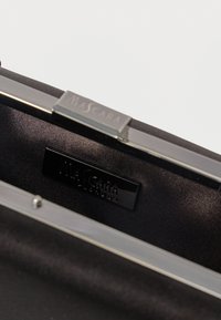 Juodas satino delninukas su elegantišku sidabro rėmeliu. Viduje yra lygus pamušalas ir juodas logotipo ženklelis su užrašu "MASCARA."