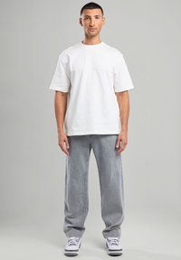 White cotton short-sleeve t-shirt paired with light grey loose-fit jeans. The outfit is complemented by white sneakers with black accents.