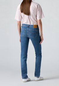 Jean en denim bleu clair avec une coupe ajustée, un délavage subtil, deux poches arrière et une étiquette logo en cuir marron sur la ceinture.