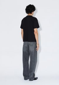 T-shirt nera in cotone e jeans grigi in denim a gamba larga. L'outfit presenta un design minimalista con una vestibilità comoda e senza motivi visibili.