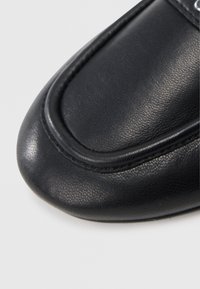 Czarny skórzany but o zaokrąglonym czubku, teksturowanej powierzchni i przeszyciach jako akcentach. Górna część wykonana z gładkiego materiału o subtelnym połysku.