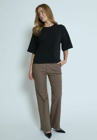 Black cotton t-shirt with short sleeves, paired with light brown tailored trousers and black pointed-toe heels, on a neutral background.