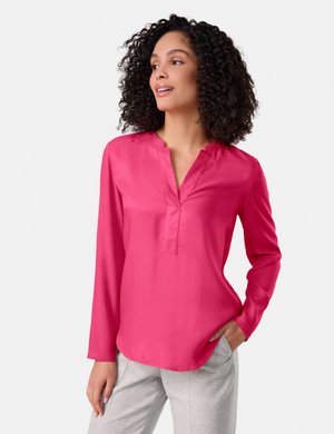 Hot pink long-sleeve shirt with a V-neck and subtle sheen. Features a relaxed fit with a rounded hem and smooth texture. Paired with light gray trousers.