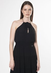 Schwarzes Halsbandkleid mit einem Rosendetail am Ausschnitt, mit einem gerafften Taillenband und einem gestuften Rockdesign. Glatte Stofftextur.