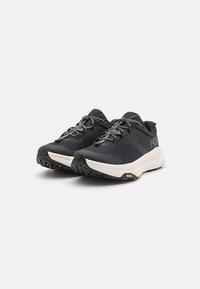 Sapatilhas atléticas pretas com um cabedal texturizado, atacadores cinzentos e uma entressola branca. Apresentam a marca Vibram na sola para maior tração.