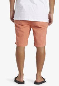 Shorts en tissu corail, de longueur mi-cuisse, dotés d'une poche arrière unique et d'une texture lisse. Associés à des sandales à glisser noires.