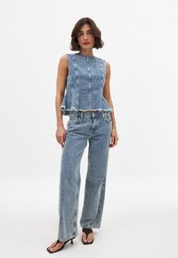 Jeansoutfit met een mouwloos topje met rafelige randen en wijde broekspijpen, beide in lichtblauw met een textuurpatroon.