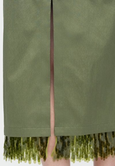 Μίντι φούστα σε ελαιί πράσινο χρώμα με σκίσιμο στο πίσω μέρος, αποκαλύπτοντας μια στρωματοποιημένη βάση από πράσινο παγιετέ ύφασμα από κάτω.