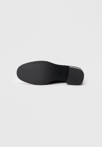 Semelle d'une chaussure habillée noire avec un talon léger, présentée à plat sur un fond blanc.