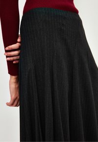 Tummanharmaa raitapikkutakki, valmistettu kevyestä kankaasta, jossa on virtaava muotoilu. Ominaisuuksiin kuuluu korkea vyötärö ja laskokset lisäämään liikkuvuutta.