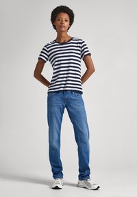 Camiseta de algodón a rayas marino y blancas con manga corta, combinada con jeans de mezclilla azul claro y zapatillas grises. Diseño simple, corte relajado.